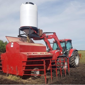 a red tractor emptying feed into a 52 bushel pallet grain bin into a creep feeder