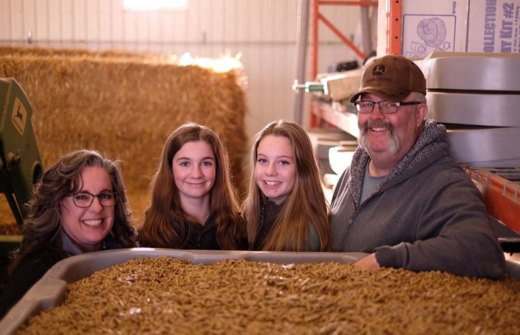 four people standing behind a 40 bushel pallet grain bin filled with grain